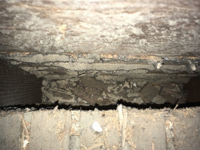 Looking into the cavity of an attic floor that was under a HVAC system. The area is tan and dirty.