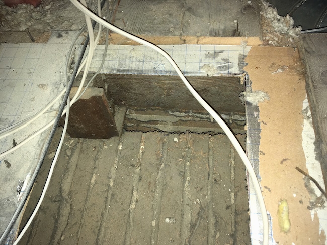 A hole in a dirty attic floor showing old white flooring where the HVAC unit was resting.