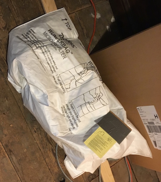 A white full vacuum bag laying on a wooden floor next to a cardboard box.