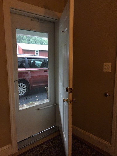 An open door with a closed storm door leading to the outside in a house.