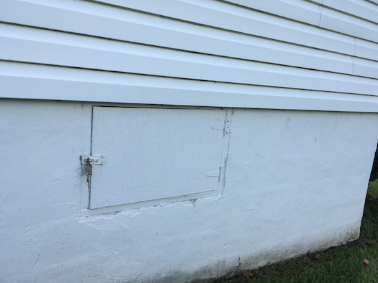 A crawl space door on the outside of a white farmhouse