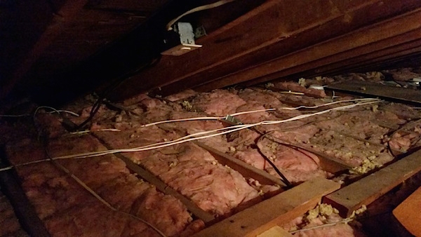 Pink fiberglass batts in-between the rafters up in an attic of a house with wires an an outlet.
