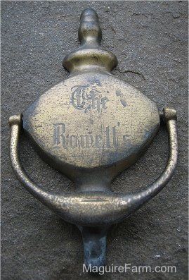 Close Up - A Door Knocker laying on a stone porch. The Words - The Rowell's - are on it