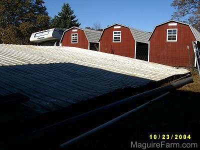 A metal tin roof that is behind a fence and there are three red storage sheds and an RV camper in the background