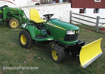 John Deere X728 Ultimate™ Tractor with a barn and another John Deere tractor behind it