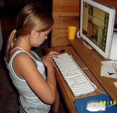 A blonde-haired girl in a white shirt is on AOL instant messenger while holding an orange and white snake in front of a This End Up computer cabinet