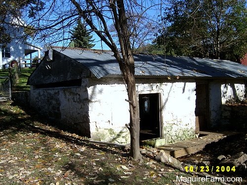 An open window and door of an old stone springhouse. There is a white farm house behind it.