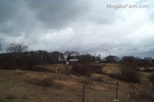 A far away view of an old 1800s white barn with a red roof surrounded by fields. 